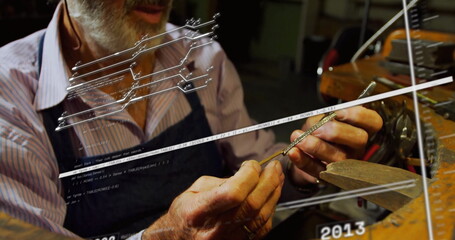 Craftsman holding metal part and filing edges at workbench with vise, wearing striped shirt, apron