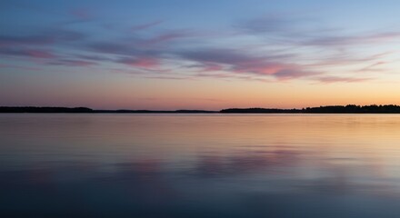 Naklejka premium Calm water reflects colorful sunset sky with clouds and distant trees.