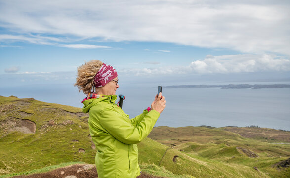 Senior woman hiking on the Isle of Skye near Old Man of Storr taking photo with smartphone by the sea