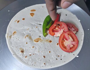 A hand places vegetables on a thin pancake