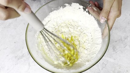 Vibrant yellow batter is being mixed in a glass bowl with a whisk, illustrating the transition from dry to wet ingredients, creating a smooth consistency