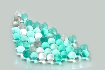 Arrangement of translucent aqua and white marbles on reflective surface with light grey background.