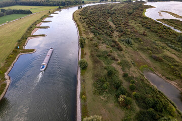 Cargo ship passing river IJssel valley with floodlands on either side. Aerial inland shipping waterway infrastructure concept