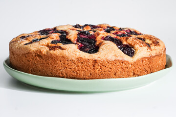 Traditional rustic plum cake with baked fruit and golden crust on a plate. Homemade dessert, whole cake close-up, sweet and fresh.