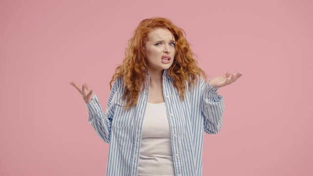 Confused red-curly haired woman shrugs shoulders showing uncertainty, confusion, hesitation