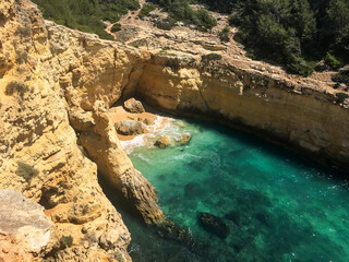 Scenic hidden cove with sandy beach, golden cliffs and turquoise water near Carvoeiro, Algarve, Portugal.