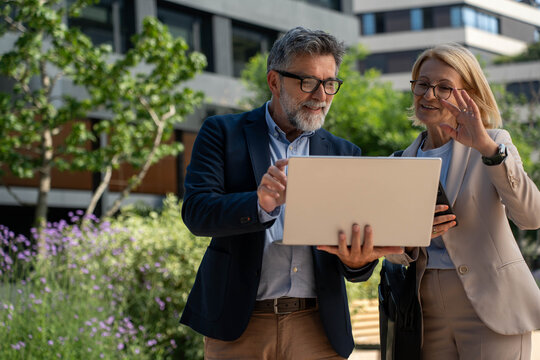 Diverse business couple collaborating on laptop outdoors in modern urban district, analyzing data and planning ideas together, teamwork.