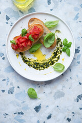 White plate with tomato bruschettas and basil oil, vertical shot on a white and blue granite background with space