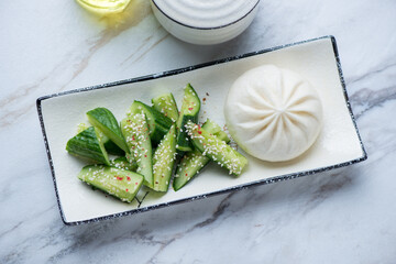 Plate with chinese steamed baozi and smashed cucumber salad, horizontal shot on a white granite...