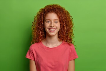 Smiling Young Woman with Red Curly Hair in Pink T-Shirt on Green Background