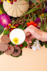 Close-up of hand holding cup of milk with flower, decorated with cookies, berries, and autumn flowers.