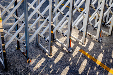 Metallic expandable gate with wheels casting shadows on asphalt surface