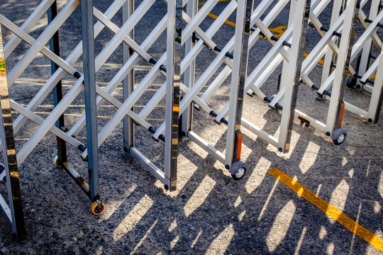 Metallic expandable gate with wheels casting shadows on asphalt surface