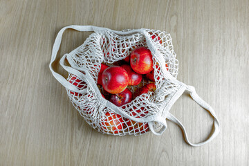 Red apples in eco-friendly mesh bag on wooden surface