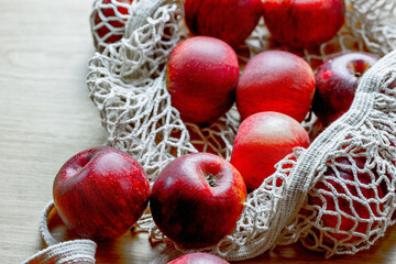 Fresh red apples in eco-friendly reusable mesh bag on wooden surface