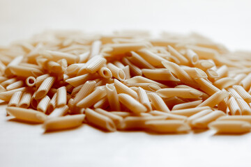 Close-up of uncooked penne pasta on white surface
