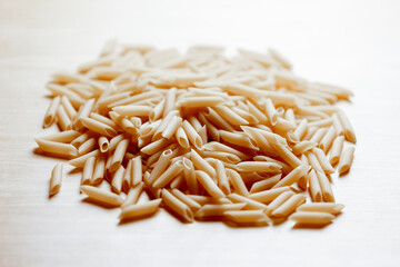 Close-up of uncooked penne pasta on light wooden surface