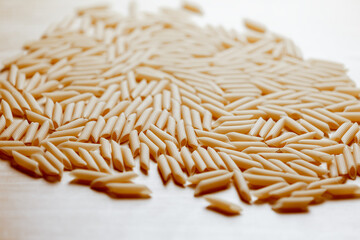 Uncooked penne pasta on wooden surface in warm light