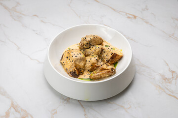 Chicken in creamy mustard sauce with black sesame, served on white marble background