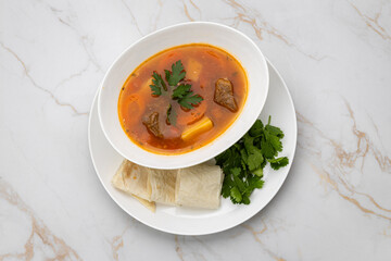 Traditional beef soup with vegetables, herbs and lavash on marble background