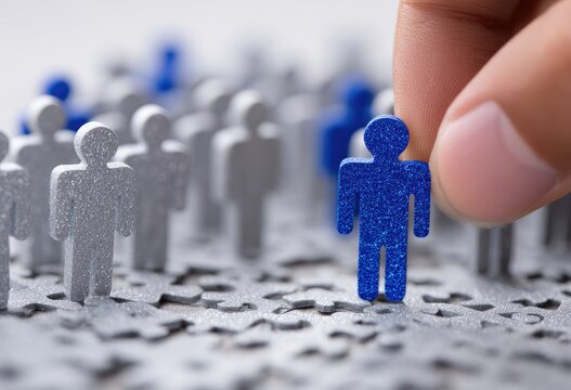 A hand places a blue figure among silver figures scattered on a surface with puzzle piece texture, focus on the chosen blue figure