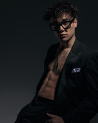 Obraz premium attractive fashion man with glasses showing abs muscles while sitting