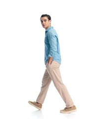 Naklejka premium side view of happy young man in blue jeans shirt walking with hand in pocket