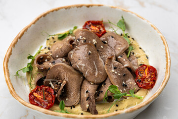 Beef tongue slices with hummus, sun-dried tomatoes and greens in ceramic bowl on marble table