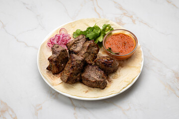 Traditional Georgian grilled meat (mtsvadi) with onion, herbs, and sauce on lavash