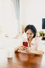Asian young female using smartphone in bright modern living room