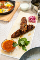 Juicy grilled lula kebab on lavash with herbs and red sauce, served on a white plate