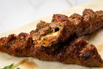 Close-up of grilled kebab with melted cheese inside on flatbread, juicy and spicy