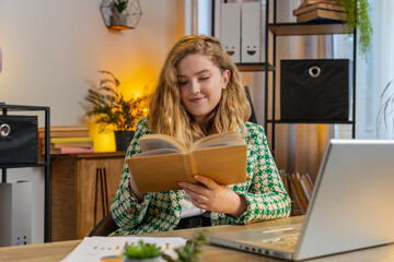 Caucasian young businesswoman reading interesting book, turning pages smiling enjoying literature,...