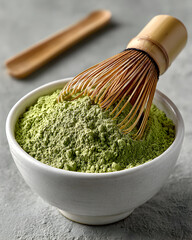 A matcha whisk in a bowl of matcha powder on a gray surface.