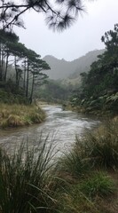 Fototapeta premium Tranquil stream winds through a forest with tall trees, grasses, and hazy mountains. A vertical shot showing natural beauty on a misty day
