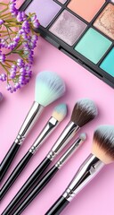 Makeup brushes and palette on pink background, with a small bouquet of flowers