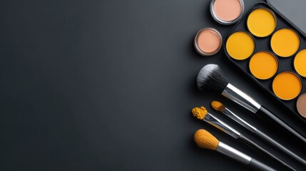 Naklejka premium An overhead shot of a makeup palette with yellow and neutral tones and brushes arranged diagonally on a dark gray background