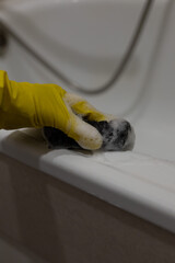 Cleaning bathtub edges with sponge and rubber gloves