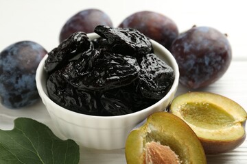 Dried prunes, fresh plums and green leaf on white wooden table, closeup