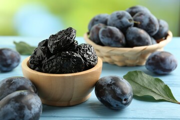 Dried prunes in bowl, leaf and fresh plums on light blue wooden table, closeup