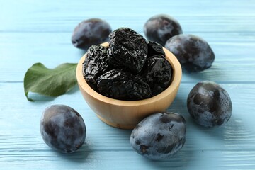 Dried prunes in bowl, leaf and fresh plums on light blue wooden table, closeup