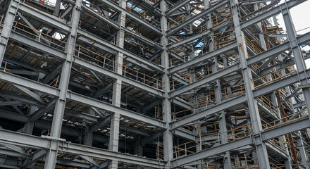 A complex network of steel beams forming the skeleton of a large industrial building under construction.