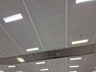 High-angle view of a modern tiled ceiling with gray grid panels, embedded fluorescent lights, and a...