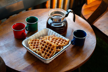 Close-up of freshly baked golden brown croffles served in a ceramic dish on a wooden table. A glass coffee pot and enamel mug complete the cozy breakfast setup.