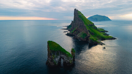 Dramatic Drangarnir cliffs and lush landscapes emerge from serene waters in the Faroe Islands during twilight. A captivating view showcases natures raw beauty and vibrant colors that inspire awe.
