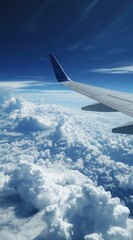 Obraz premium Airplane wing slicing through fluffy white clouds under a vivid blue sky, captured from inside the cabin