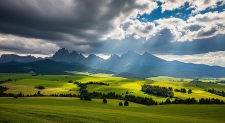Sunbeams breaking through dramatic clouds over rolling green hills and jagged mountains