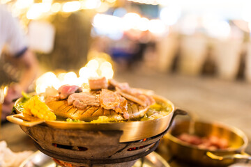 Mookata, Thai BBQ grill pork dish. The round hot pan with pork is grilled on top. Flavorful dish for sharing.