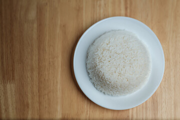 flat lay top view shot of streamed white Thai's jasmine rice in the white clean dish isolated put on the wooden plate dinner table closed to one conner of the photo with empty copy space for texts