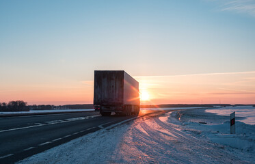 Semi truck driving along a snowy highway at sunset in winter © Evgenii Bakhchev